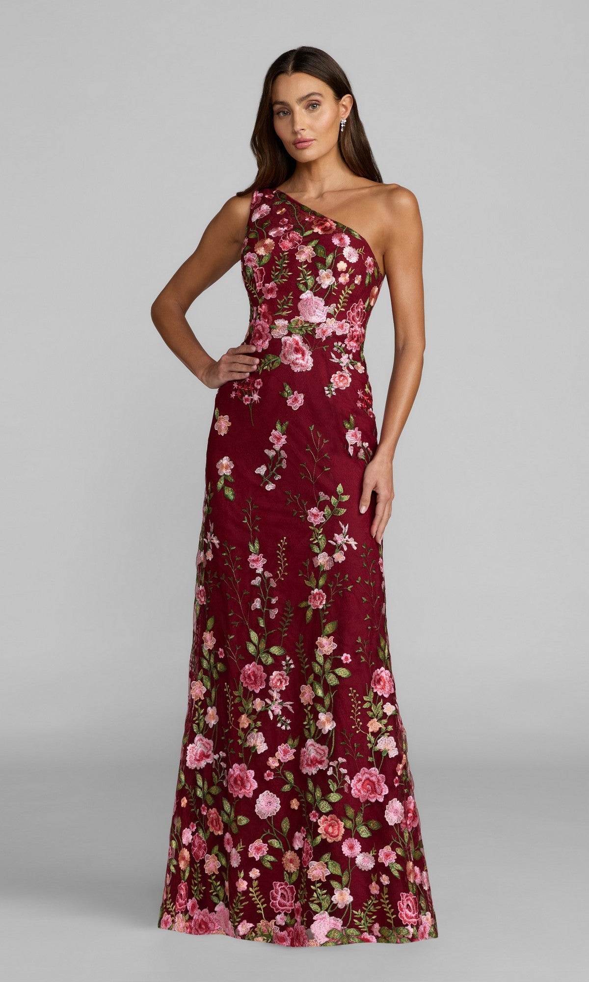 A woman stands against a plain gray background wearing the Mac Duggal 68606 Long Floral-Print Formal Dress, a sleeveless, floor-length maroon maxi with pink and green floral embroidery.